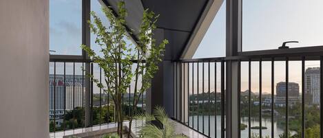 A balcony with a view of a lake and buildings, featuring a potted plant arrangement and a metal railing.