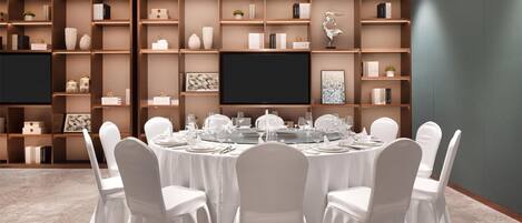 A conference room with a round table, white chairs, and a bookshelf with various items.