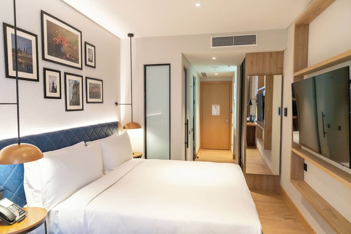 Habitación de hotel con una cama grande, televisión, escritorio con lámpara y cuadros en la pared.