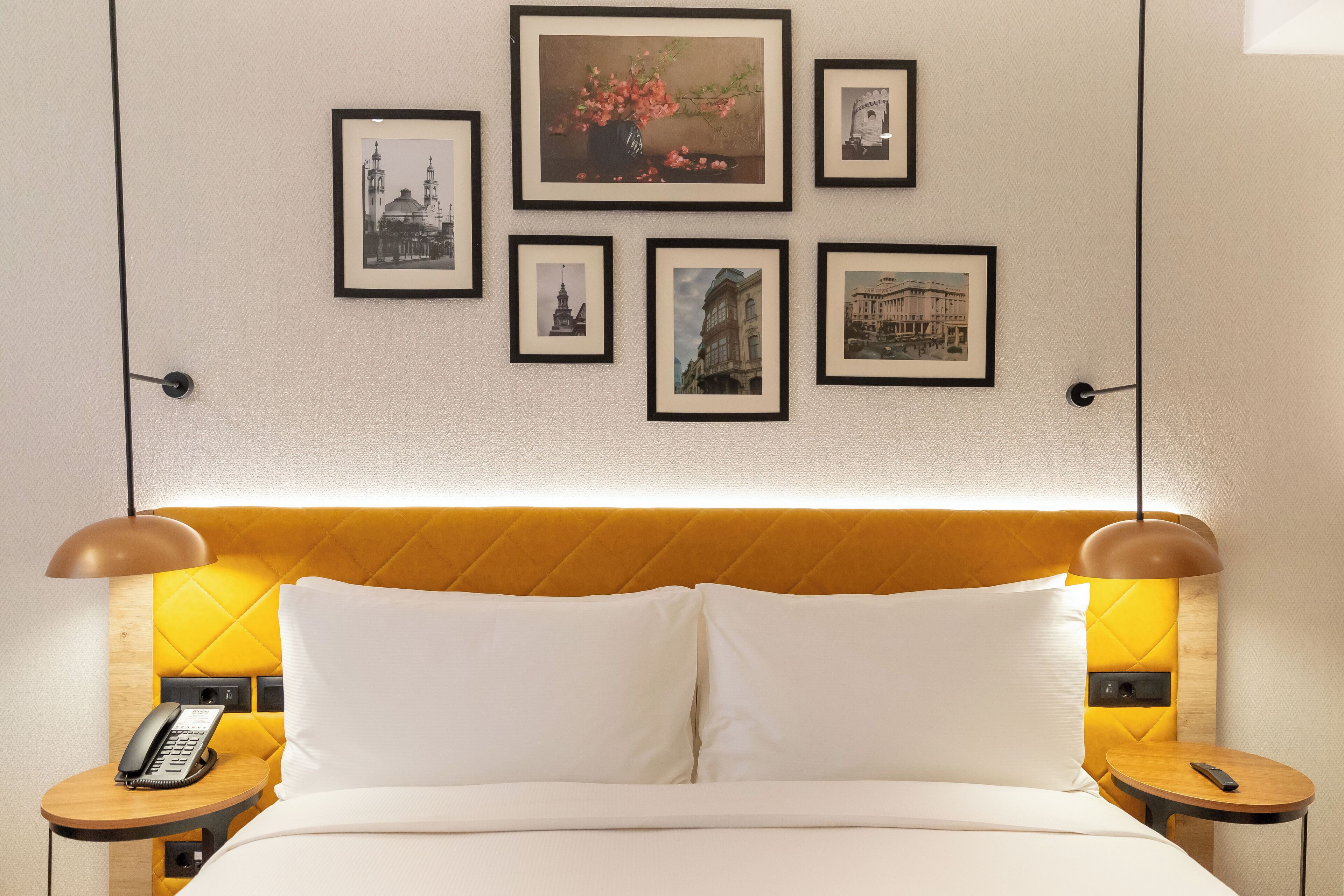 Une chambre d’hôtel avec un lit, des tables de chevet, un téléphone et des tableaux encadrés au mur.