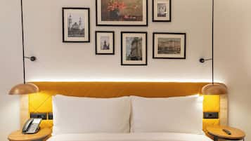 Une chambre d’hôtel avec un lit, des tables de chevet, un téléphone et des tableaux encadrés au mur.