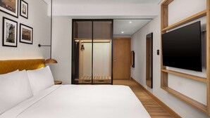 Une chambre d’hôtel moderne avec un grand lit, un téléviseur fixé au mur et un placard à portes coulissantes.