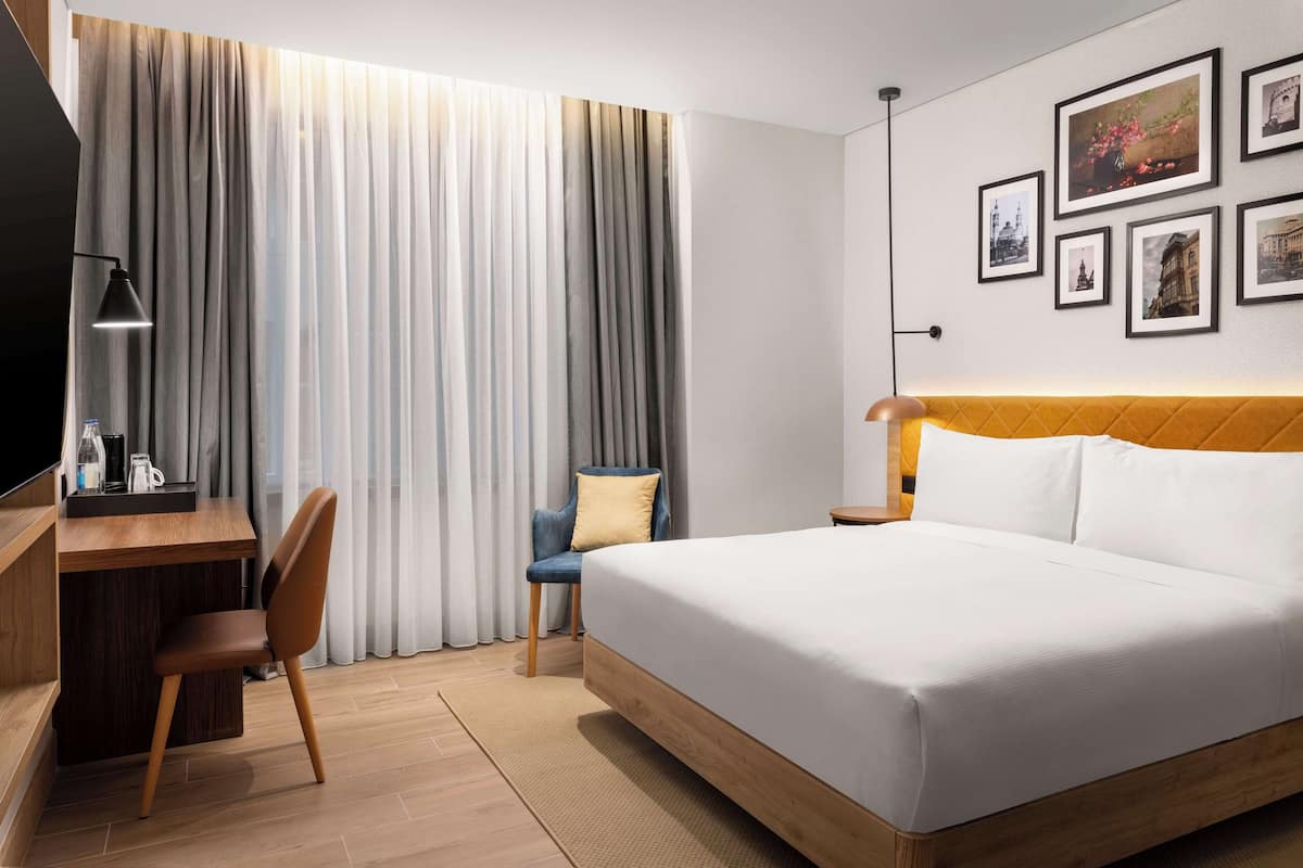 Una habitación de hotel con cama, escritorio, silla, televisor y una pared decorada con cuadros.