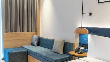 Ein modernes Hotelzimmer mit einem blauen Sofa, einem Holzkopfteil, einem Nachttisch mit Lampe und einem Telefon.