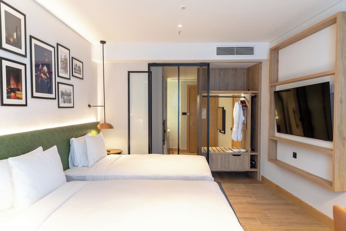 Una habitación de hotel moderna con una cama grande, un vestidor, un televisor y cuadros en la pared.