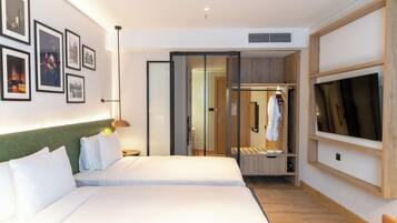 A modern hotel room with a large bed, a walk-in closet, a TV, and framed pictures on the wall.