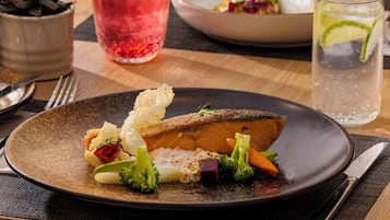 A plate of food with vegetables and a piece of meat, a glass of red drink, and a glass of clear drink with a lime slice.