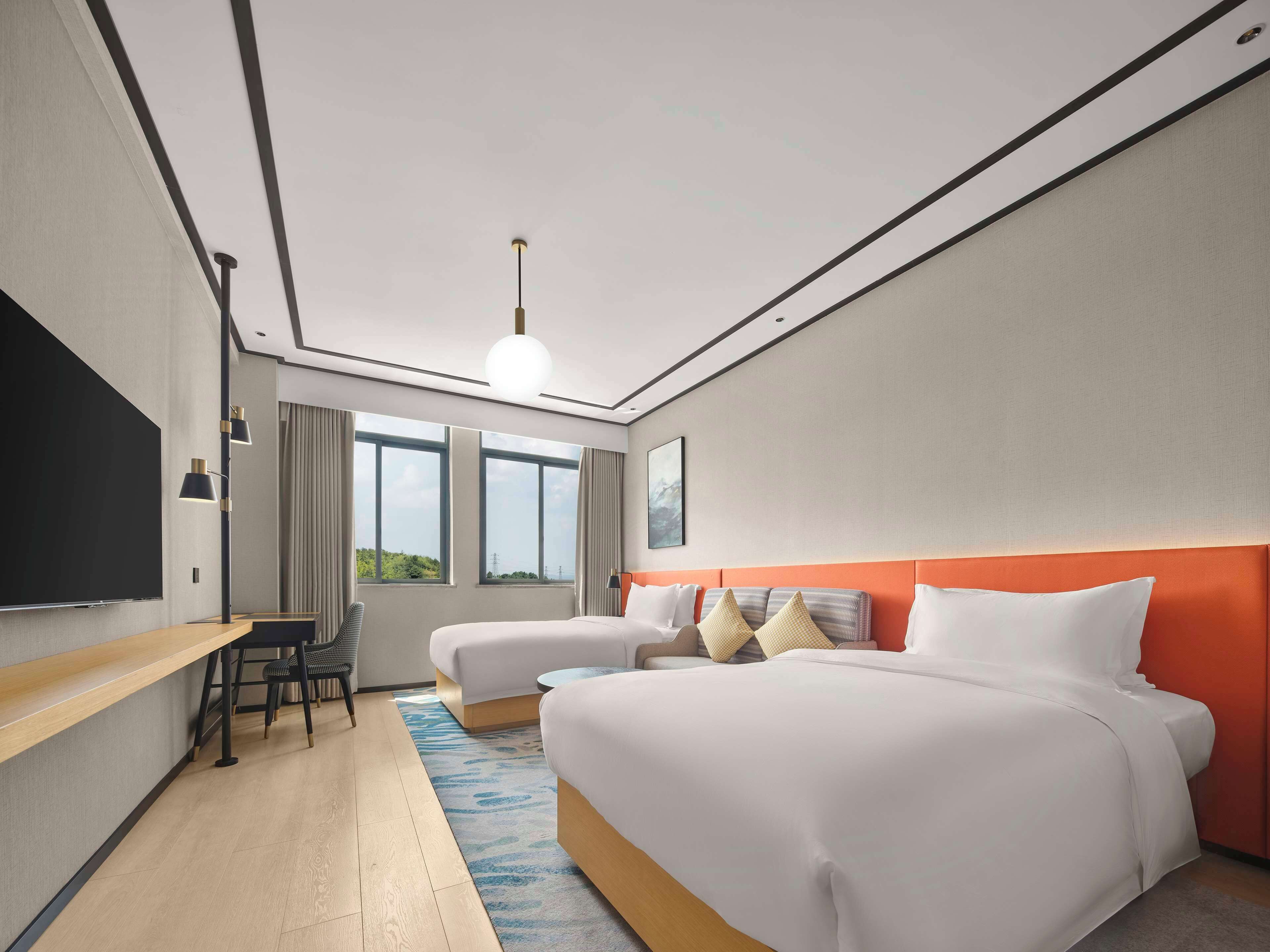 A hotel room with a large bed, a desk, a chair, and a TV.
