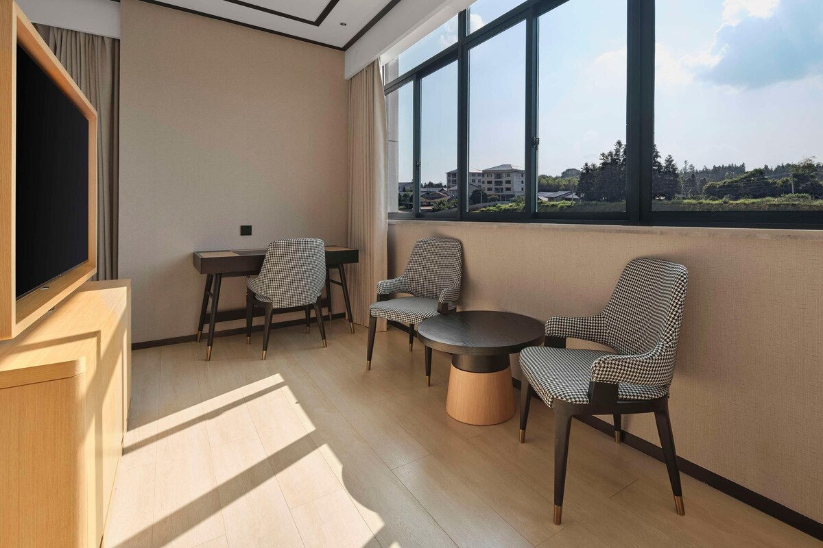 A modern room with a large window, a flat-screen TV, and three patterned chairs around a small table.