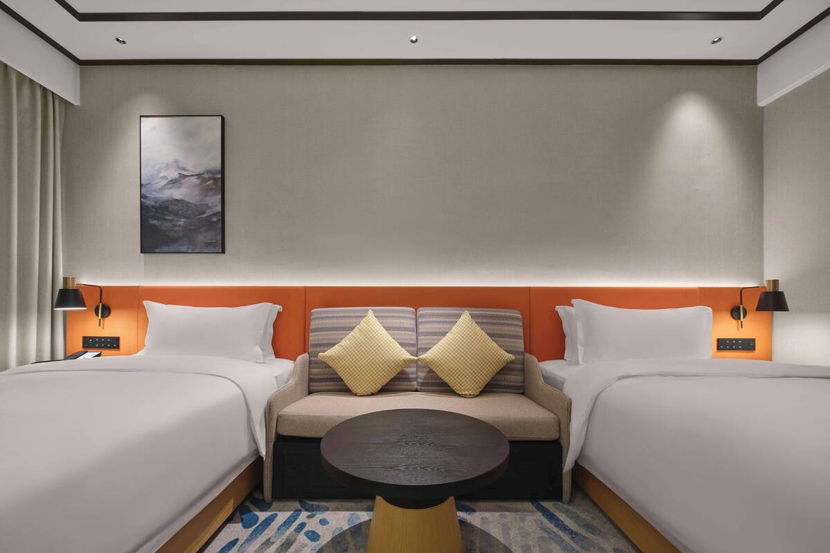 A hotel room with two beds, a sofa, a round table, and a painting on the wall.