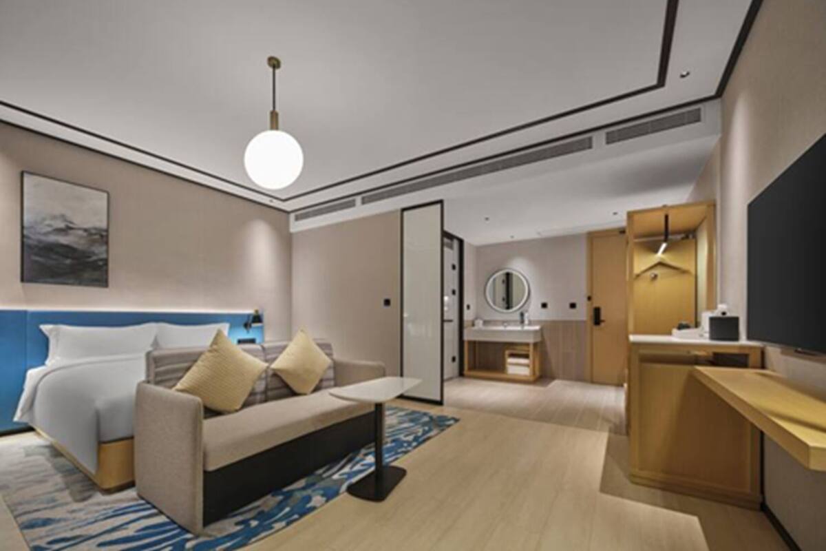 A modern hotel room with a bed, a sofa, a desk, a mirror, and a television.