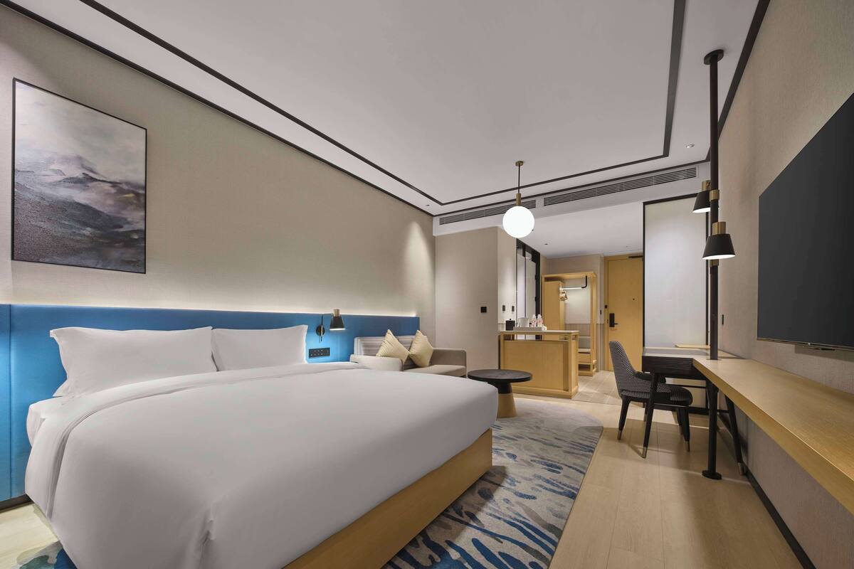 A modern hotel room with a large bed, a desk, and a chair.