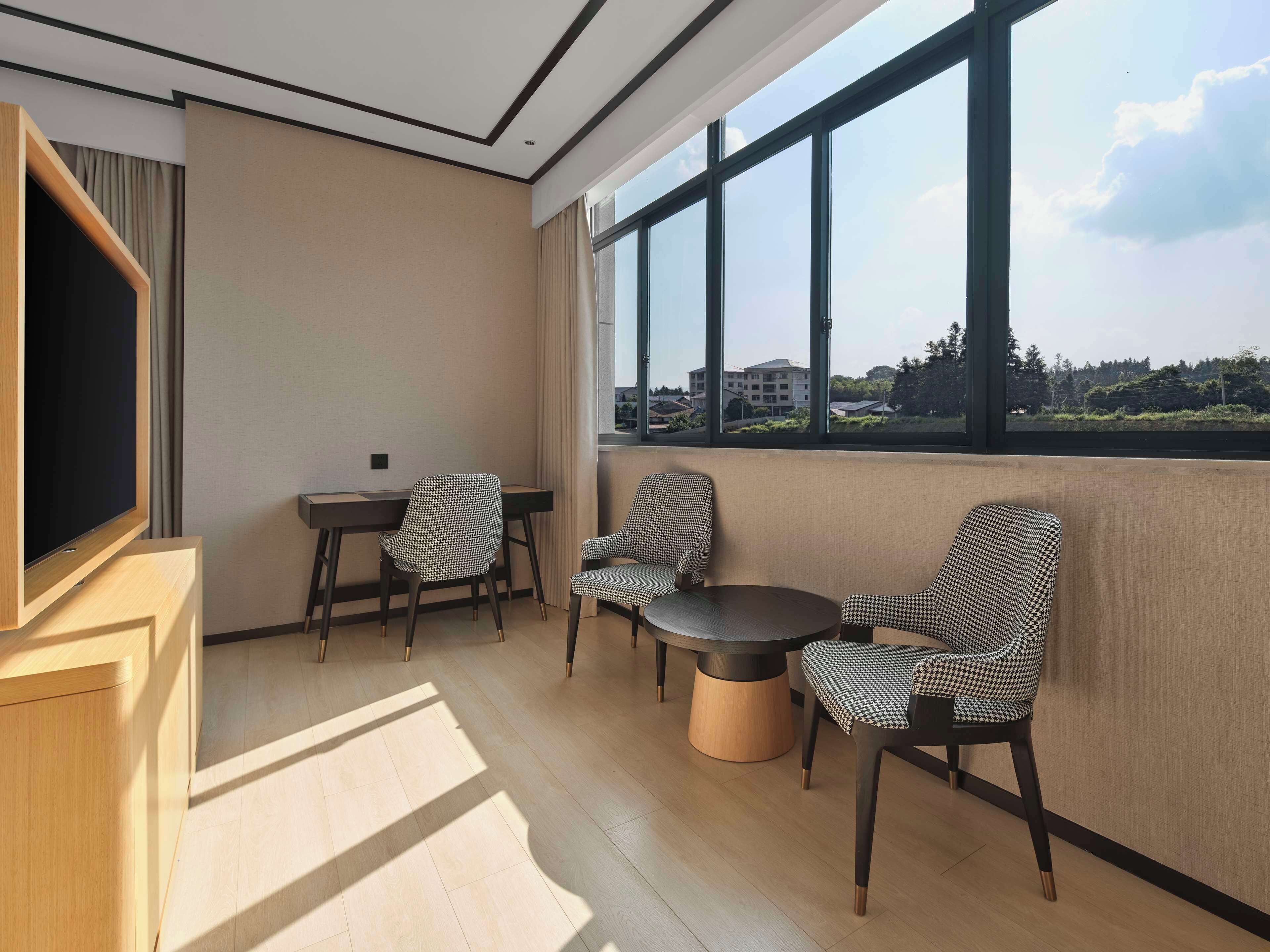 Quarto moderno com uma grande janela, televisão de tela plana e mesa redonda com cadeiras.