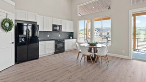 A modern kitchen with white cabinets, a black refrigerator, and a dining area with a round table and chairs. - Modern 2024 build, in welcoming Lava Hot Springs. Top unit. (Lava Hot Springs)