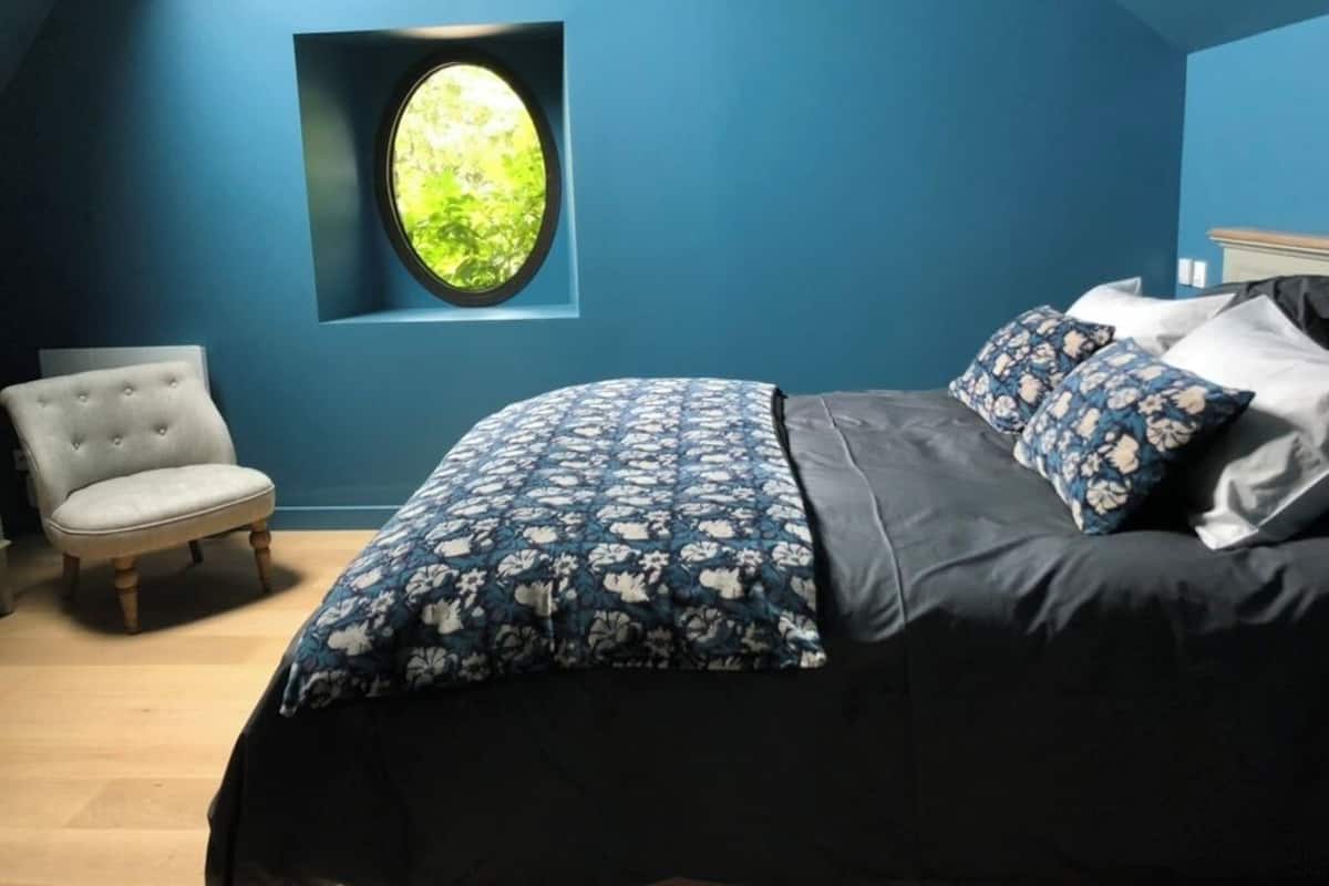 A bedroom with a large bed, a window with a view of greenery, a chair, and a dresser.