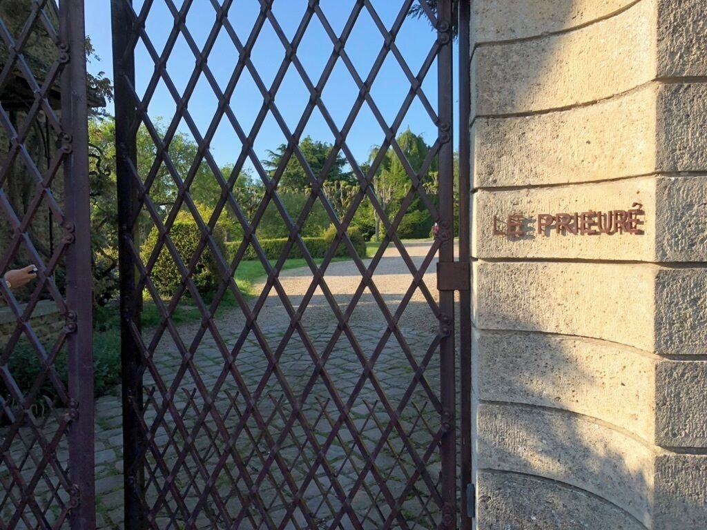 Una reja de hierro forjado con un muro de piedra y una placa que dice "LE PRIEURE".