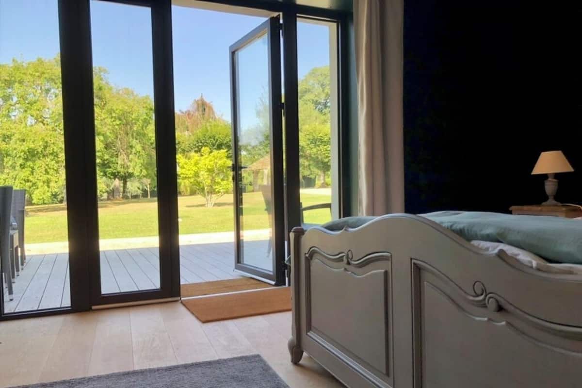 A bedroom with a bed, a window, and a view of a garden.