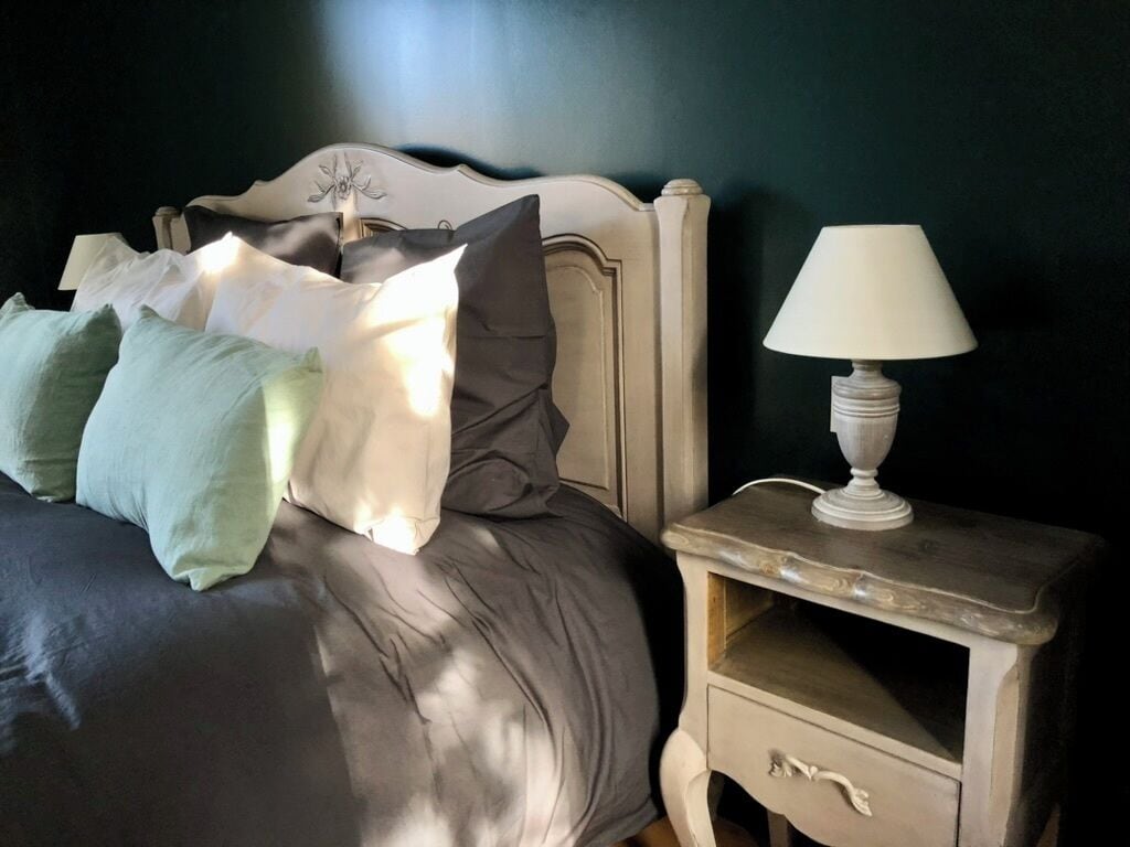 Una cama con cabecera, almohadas y una mesita de noche con lámpara.