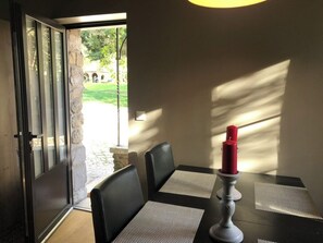 Ein Essbereich mit Tisch und Stühlen, einer Kerze auf dem Tisch und Blick ins Freie durch eine Glastür.