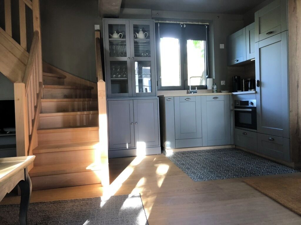 A kitchen with grey cabinets, a wooden staircase, and a window allowing natural light.