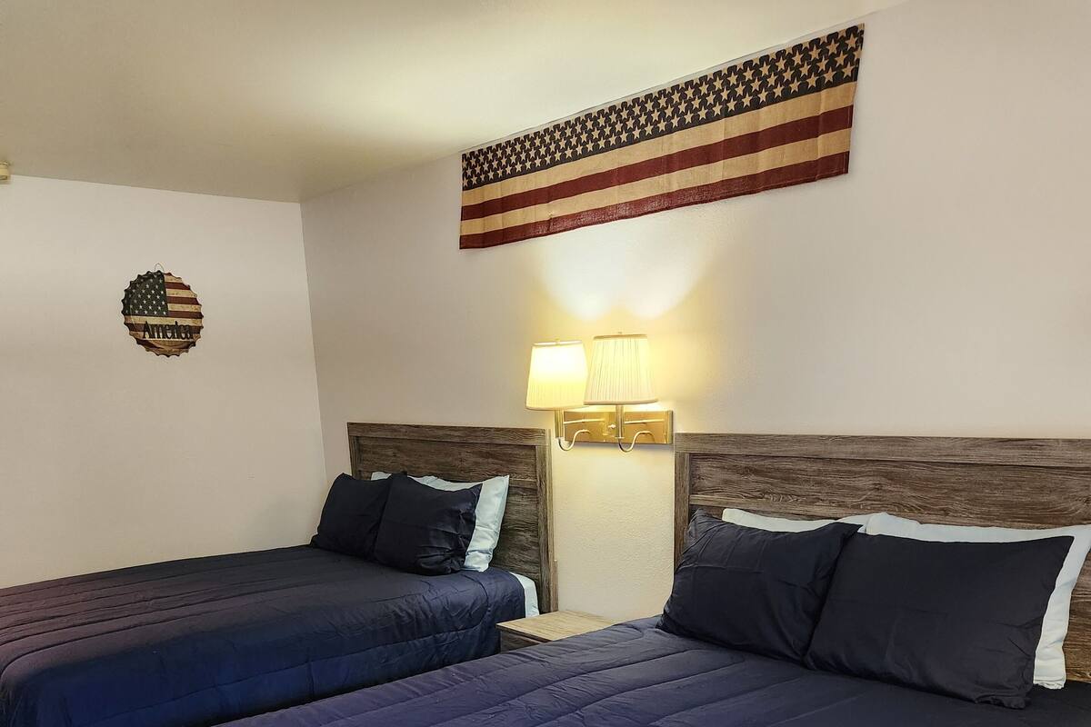 Une chambre d’hôtel avec deux lits, des têtes de lit en bois et un drapeau américain accroché au mur.
