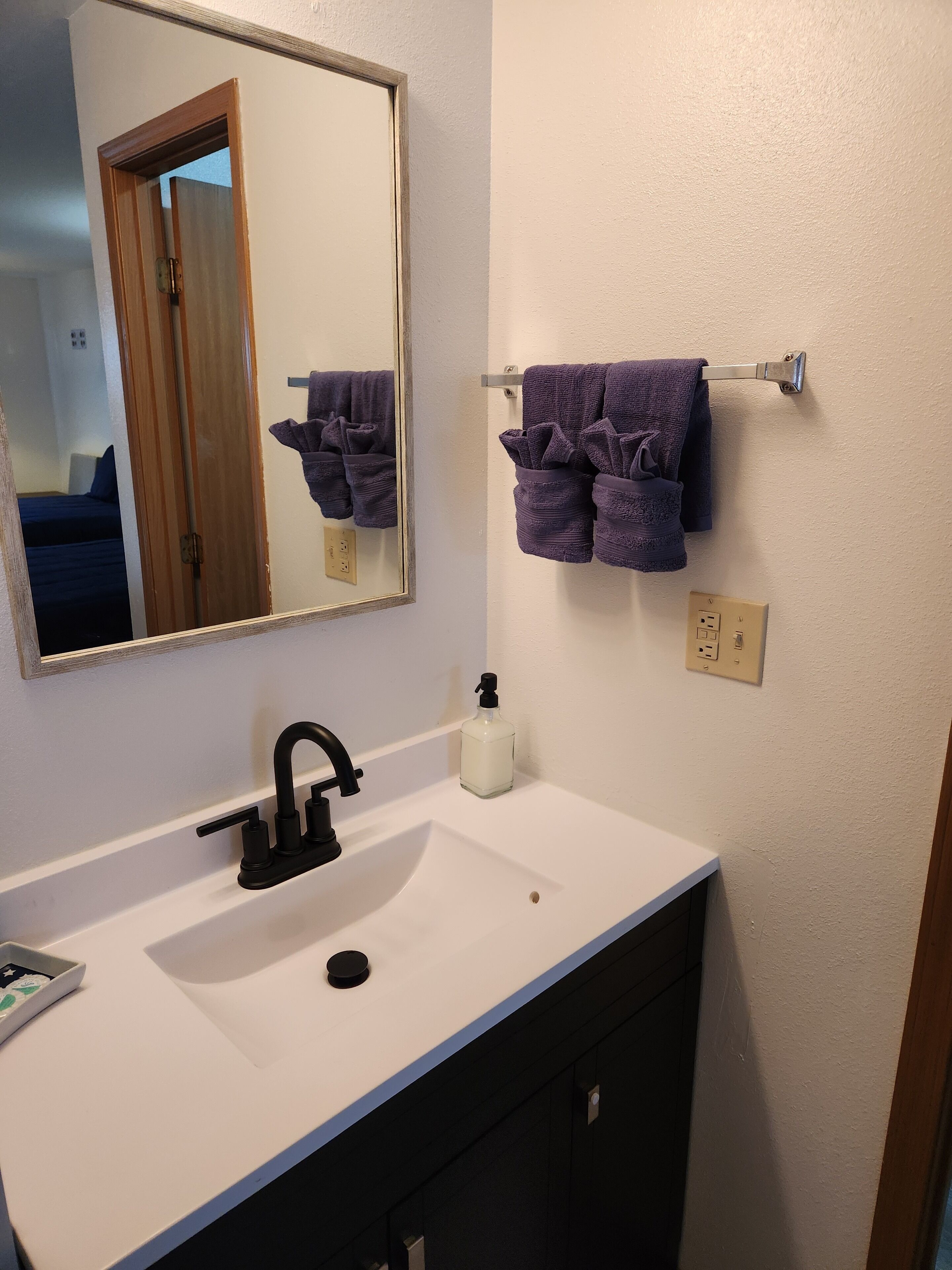 A bathroom with a white sink, a black faucet, a mirror, and a towel rack with two purple towels.