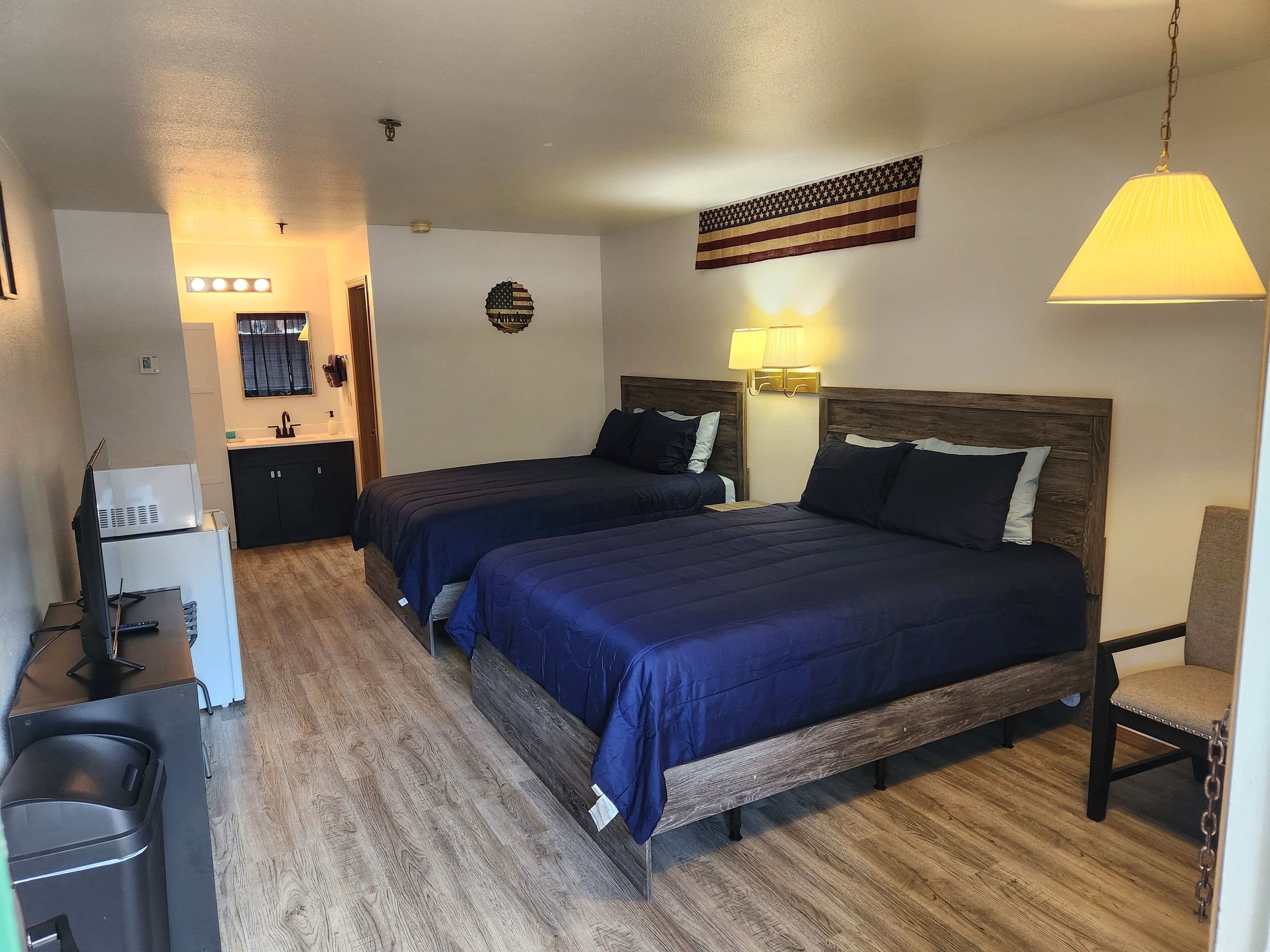 Hotelkamer met twee bedden, een bureau, een stoel, een kleine kitchenette en een Amerikaanse vlag aan de muur.