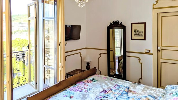 A bedroom with a bed, a chandelier, a mirror, a TV, and a door. - B&B Salerno Royal Suite Central Station (Salerno)