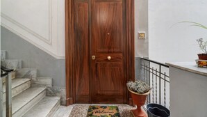 A wooden door with a brass handle, a doormat with the word "Welcome," a potted plant, and a metal railing. - B&B Salerno Royal Suite Central Station (Salerno)
