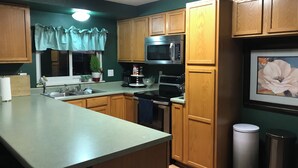Una cocina con armarios de madera, un microondas de acero inoxidable, una estufa, un fregadero y un cubo de basura.