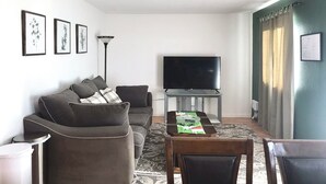 Una sala de estar con un sofá, un televisor de pantalla plana, una mesa de comedor y una alfombra estampada.