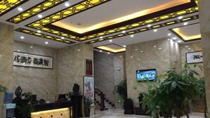Een hotel lobby met een receptiebalie, marmeren wanden, een trap en een televisiescherm.