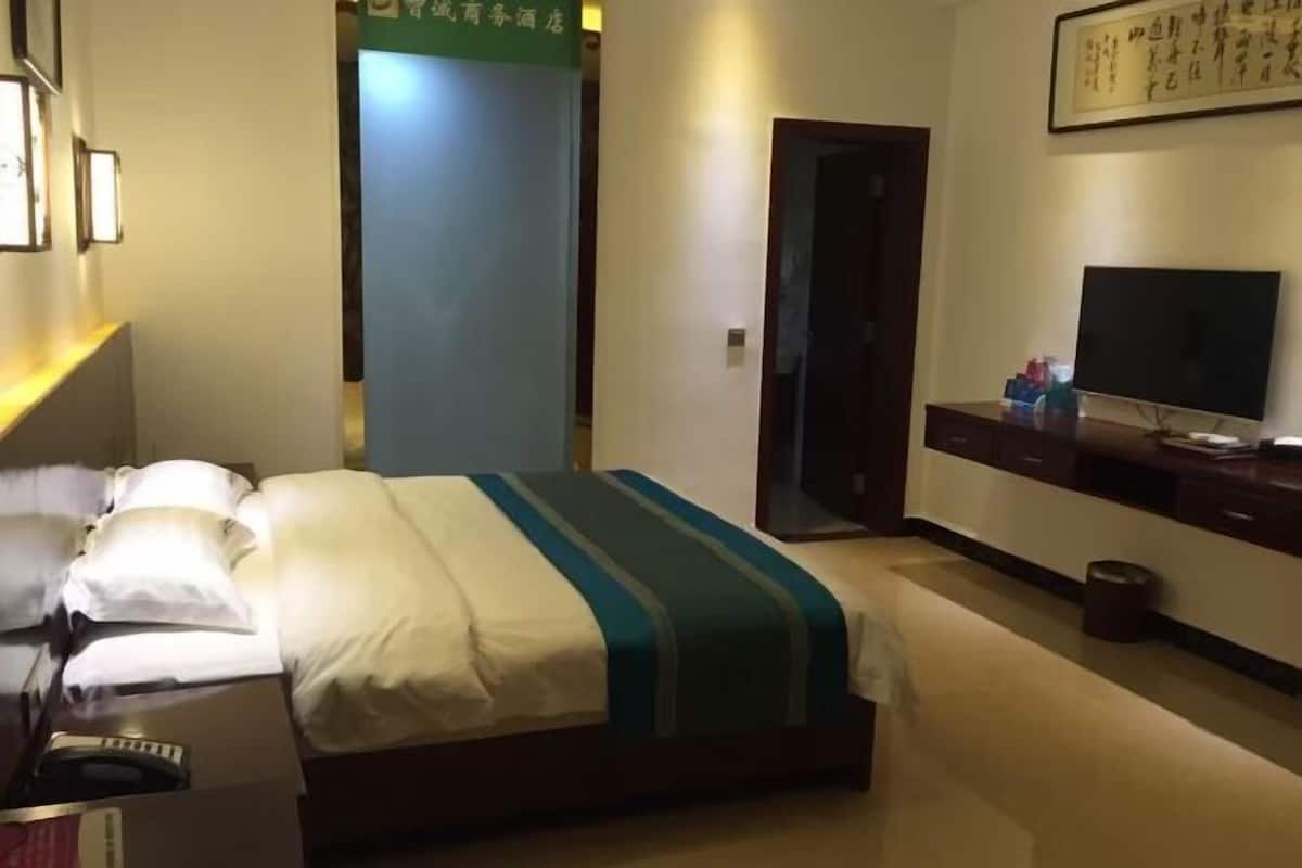 Hotellihuone, jossa on sänky, televisio, työpöytä ja peili.