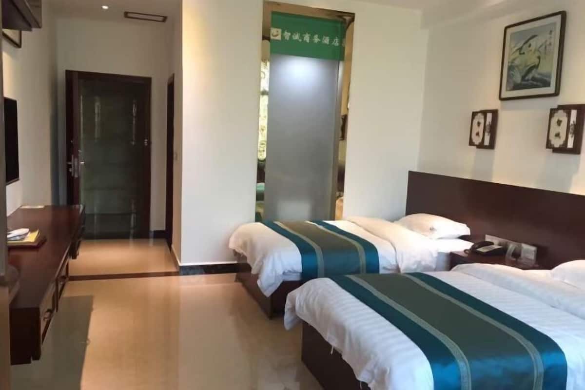 Hotellihuone, jossa on kaksi sänkyä, työpöytä ja vihreä kyltti seinällä.