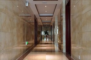 A long, polished hallway with marble walls and a reflective floor, leading to a central area with a plant and a door. - Zhicheng Business Hotel (Jianghua)