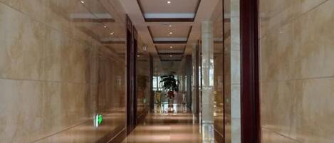 Um corredor com piso lustroso, teto refletor e portas de vidro de um lado.
