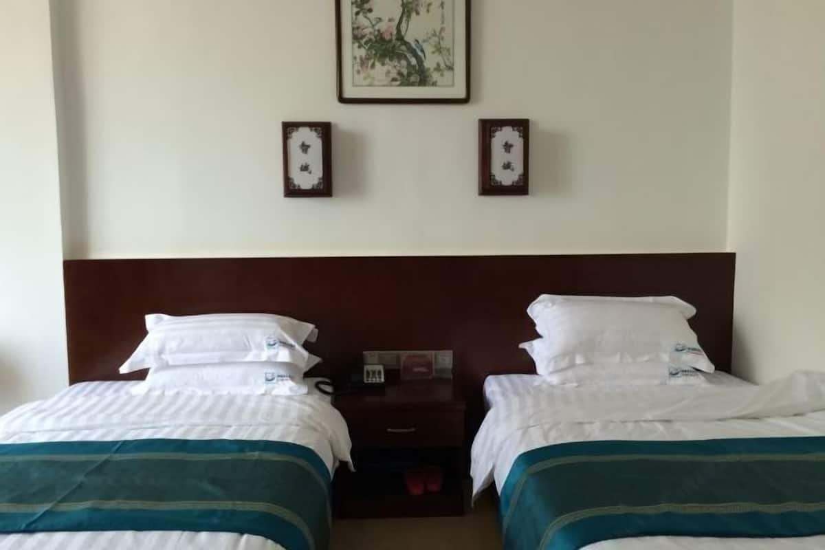 Hotellihuone, jossa on kaksi sänkyä, puinen pääty, yöpöytä lampun kanssa ja seinällä kehystetty kuva.
