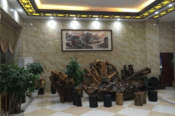 A lobby with a marble floor, a large framed artwork, and a central sculptural piece surrounded by potted plants.