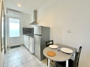 A compact kitchen with a refrigerator, stove, and sink. There is a dining table with chairs and a small rug. - Le Sully, City Center Studio with A/C (Nîmes)