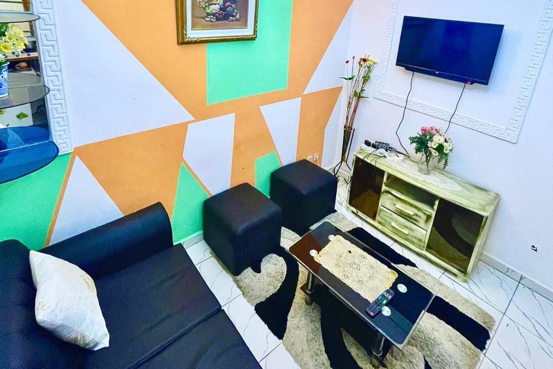 A living room with a sofa, two black ottomans, a coffee table, and a TV mounted on the wall.