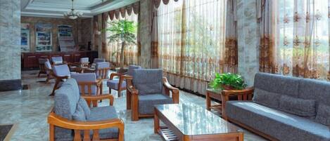 A spacious lobby with a marble floor, wooden furniture, and large windows with curtains.