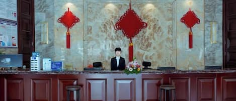 A reception desk with a marble wall, red decorations, and a computer monitor.