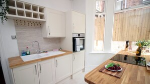 A modern kitchen with white cabinets, a wooden countertop, a sink, and a built-in oven. - Cathedral House by Tŷ SA (Newport)