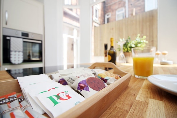 A breakfast tray with pastries and a glass of orange juice on a wooden table in a kitchen with a window view.