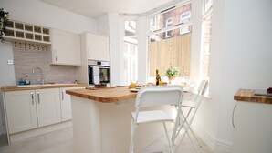 A modern kitchen with white cabinets, a wooden countertop, a built-in oven, and a window overlooking a brick building. - Cathedral House by Tŷ SA (Newport)