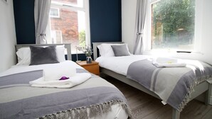 A hotel room with two beds, a nightstand, a lamp, and a window with curtains. - Cathedral House by Tŷ SA (Newport)
