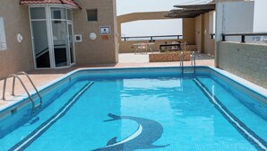 Una piscina con decorazione a forma di delfino, una zona relax esterna coperta e un ingresso con porta in vetro.