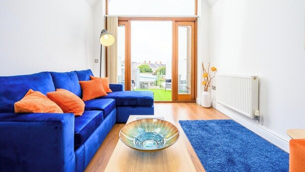 A living room with a blue sofa, a glass bowl on a wooden table, and a view through a large window. - 2 bed with terrace - Llandaff Lofts by Tŷ SA (Cardiff)