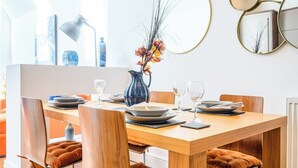 A dining area with a wooden table set for two, a vase with flowers, and modern decor including a lamp and mirrors. - 2 bed with terrace - Llandaff Lofts by Tŷ SA (Cardiff)