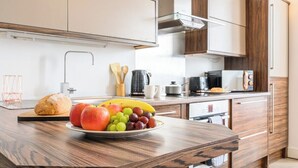 A modern kitchen with wooden cabinets, a stainless steel range hood, and a fruit bowl on the counter. - 2 bed with terrace - Llandaff Lofts by Tŷ SA (Cardiff)